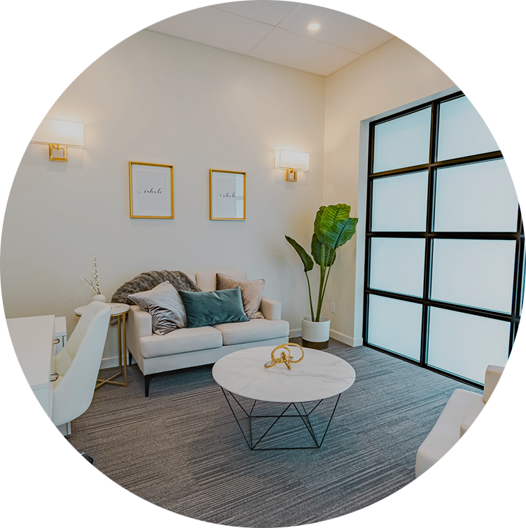 A cozy room with a loveseat, a plant in the corner, a round table in the middle, and frosted windows